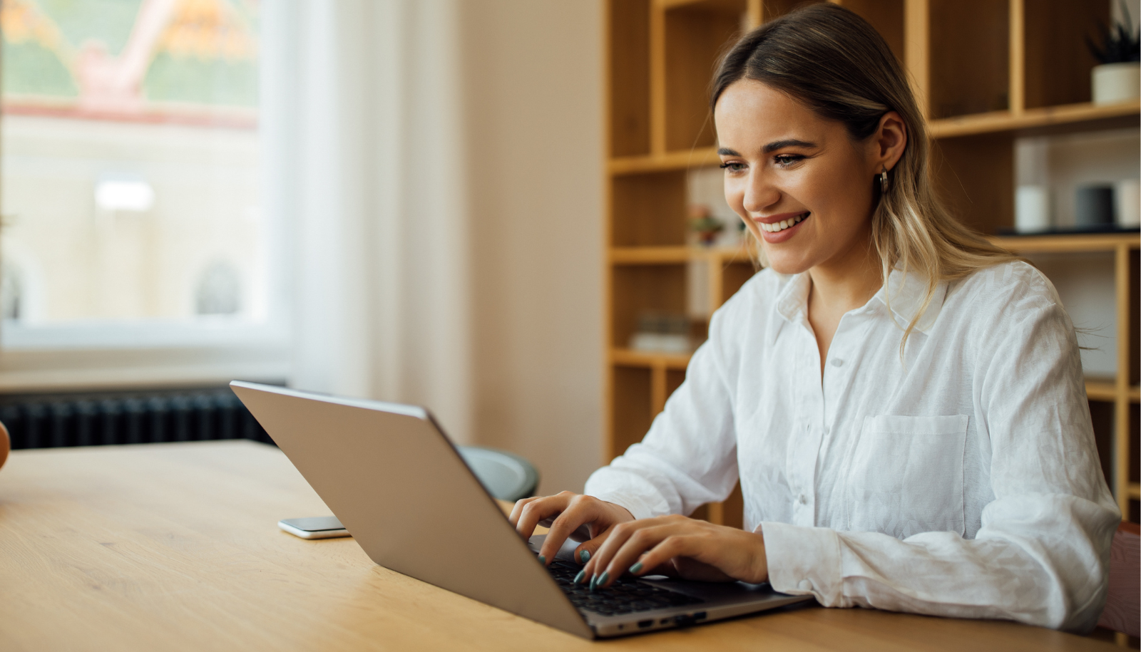 A woman wearing white shirt working at the laptop in the office. She is smiling while looking at the laptop.