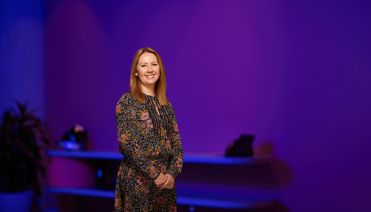 Nicole Vongdara, Senior Manager, Diversity and Inclusion at PwC standing in a floral dress in front of a purple wall