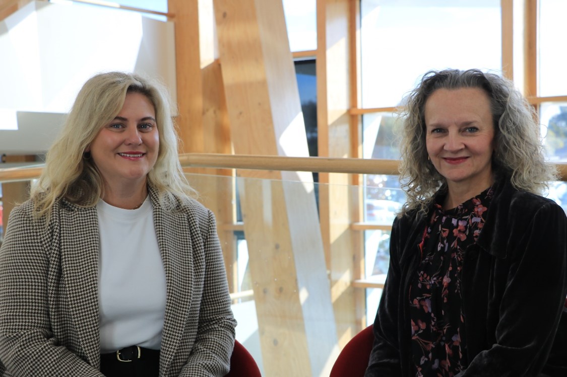 Georgia Miller and Clare Amies seated together smiling in office space.