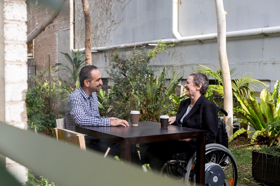 A man and woman are having a conversation over coffee, while seated outdoors.