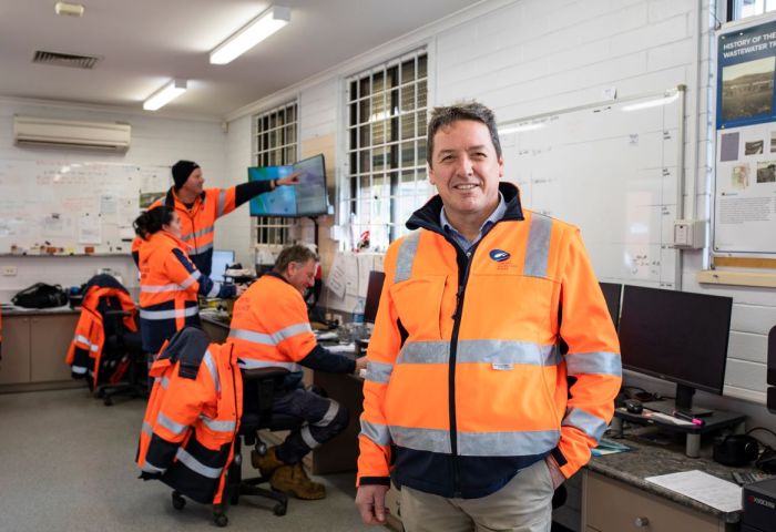 Central Highlands Water (CHW) employees are in orange hi-vis jackets, working in office. One of the employees is smiling and looking at the camera.