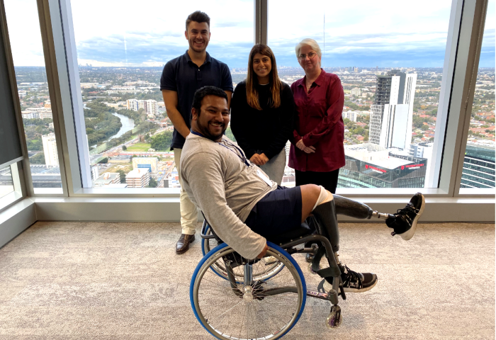 Man in wheelchair raising his leg with 3 people standing behind him 