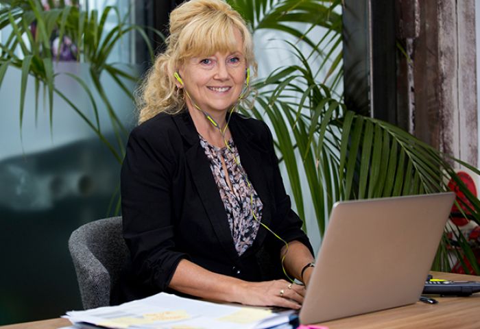 Woman sitting at desk, with a screen in front of her and wearing earphones