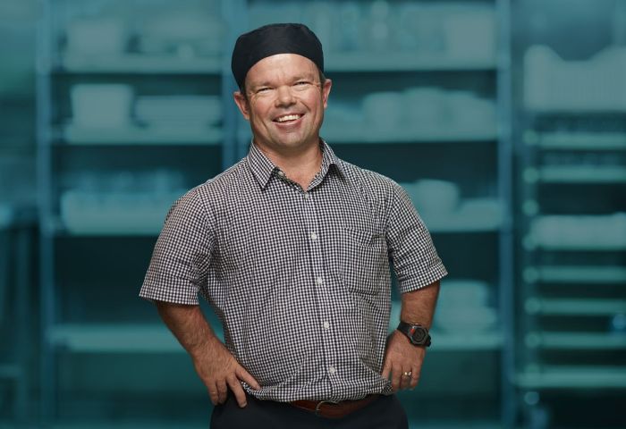 Kevin Green standing in a button-up shirt and a bakers cap