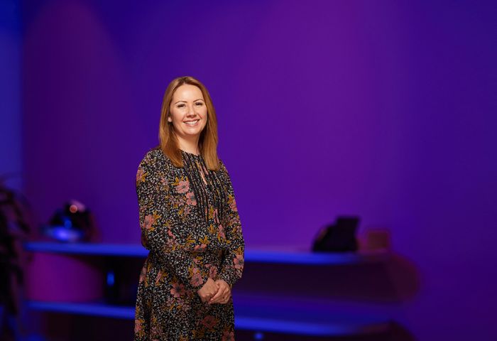 Nicole Vongdara, Senior Manager, Diversity and Inclusion at PwC standing in a floral dress in front of a purple wall