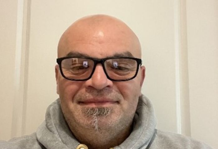 Michael standing in front of wall, wearing a jumper and glasses, smiling at camera.