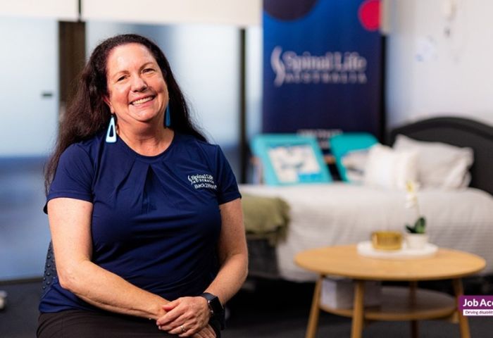 Woman sitting in a chair with bed and coffee table behind her.