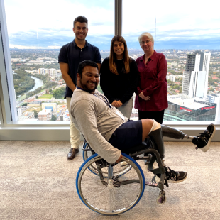 Man in wheelchair raising his leg with 3 people standing behind him 