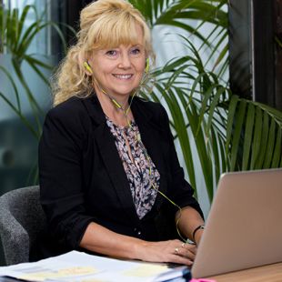 Woman sitting at desk, with a screen in front of her and wearing earphones