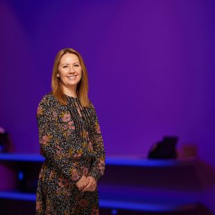 Nicole Vongdara, Senior Manager, Diversity and Inclusion at PwC standing in a floral dress in front of a purple wall