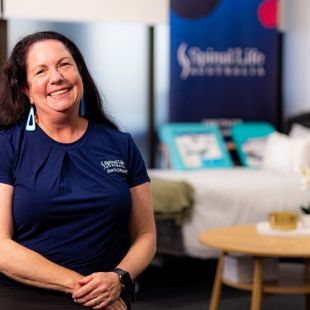 Woman sitting in a chair with bed and coffee table behind her.