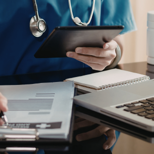 Image of a person hand writing on a pd with a opened laptop in front of them